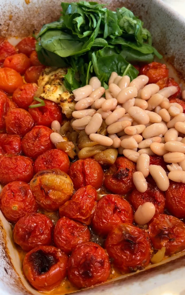 Adding cooked orzo pasta to baked tomatoes and spinach in a dish.