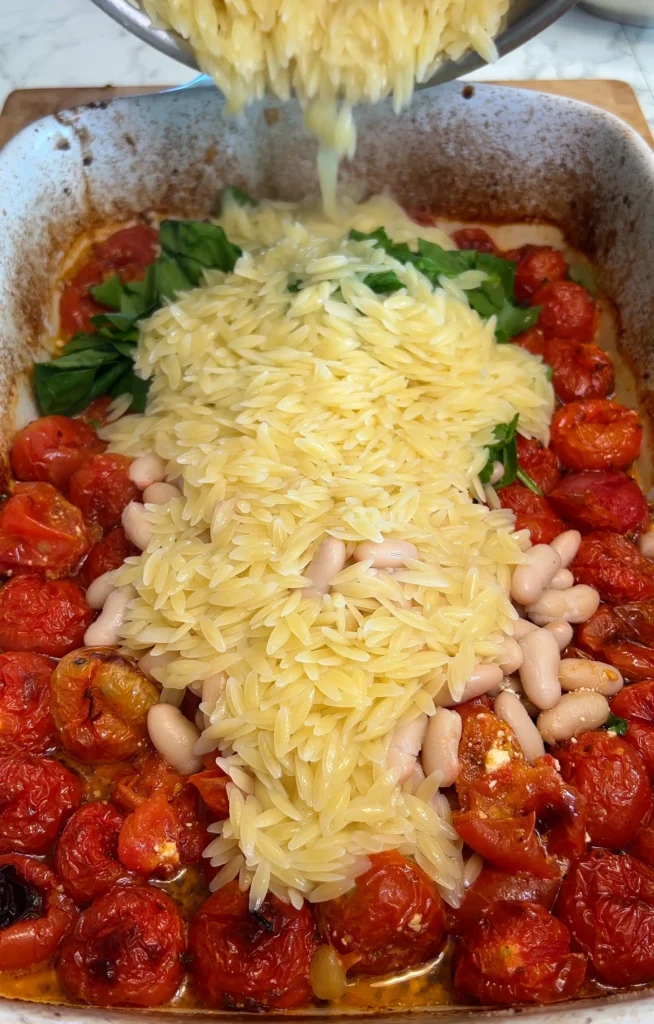 Mixing together baked orzo pasta, tomatoes, spinach, and feta in a creamy sauce.