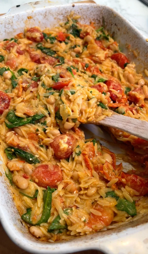 Final presentation of baked orzo pasta with spinach, tomatoes, and beans, garnished with parmesan.